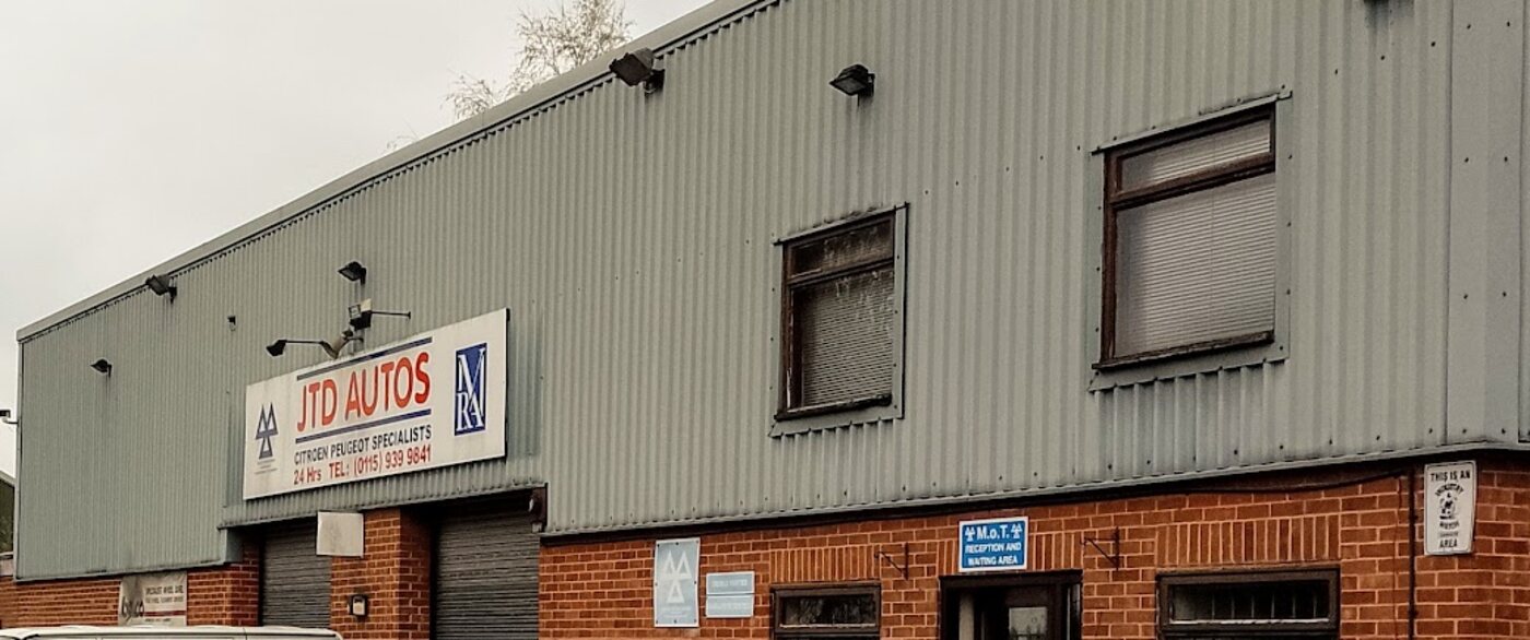 The front of Cloudside Garage on Ilkeston Road: a grey clad workshop over red brick, with the JTD Autos sign above the roller shutter and an MOT reception and waiting area sign beside the door.